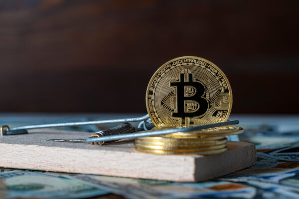 Cryptocurrency fraud: Bitcoin sitting on a mousetrap implying a scam