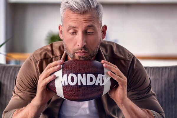 Image of sad, tired man holding football with the word "Monday" on it